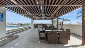An outdoor patio with a pergola, seating area, and a view of the pool and cityscape. - Marina view and 3 min from beach (Nuevo Vallarta)