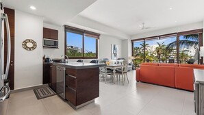 A modern kitchen with a central island, dining area with chairs, and a bright living space with a view of palm trees. - Marina view and 3 min from beach (Nuevo Vallarta)