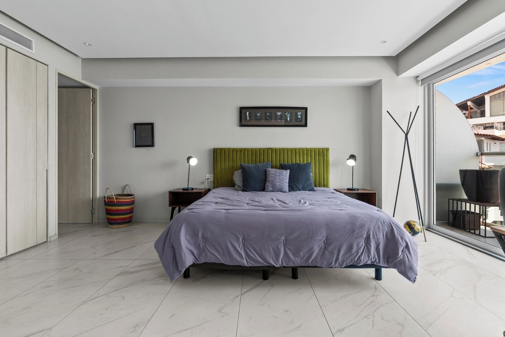 Un dormitorio moderno con una cama, mesitas de noche, cabecero verde, un ventanal y vistas al exterior.
