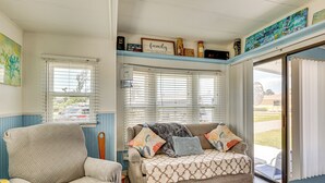Ein gemütliches Wohnzimmer mit einer Couch und einem Sessel, einem Fenster mit Jalousien und einer zur Außenwelt führenden Tür.