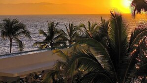 Vista al atardecer desde un balcón con palmeras y el océano.