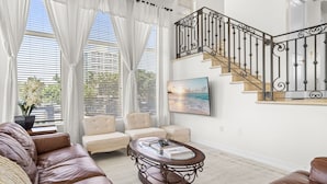 A spacious living room with a leather sofa, a round coffee table, and a staircase with ornate railings. - Birch Road Beach House | Oceanfront | Luxury Villa (Fort Lauderdale)