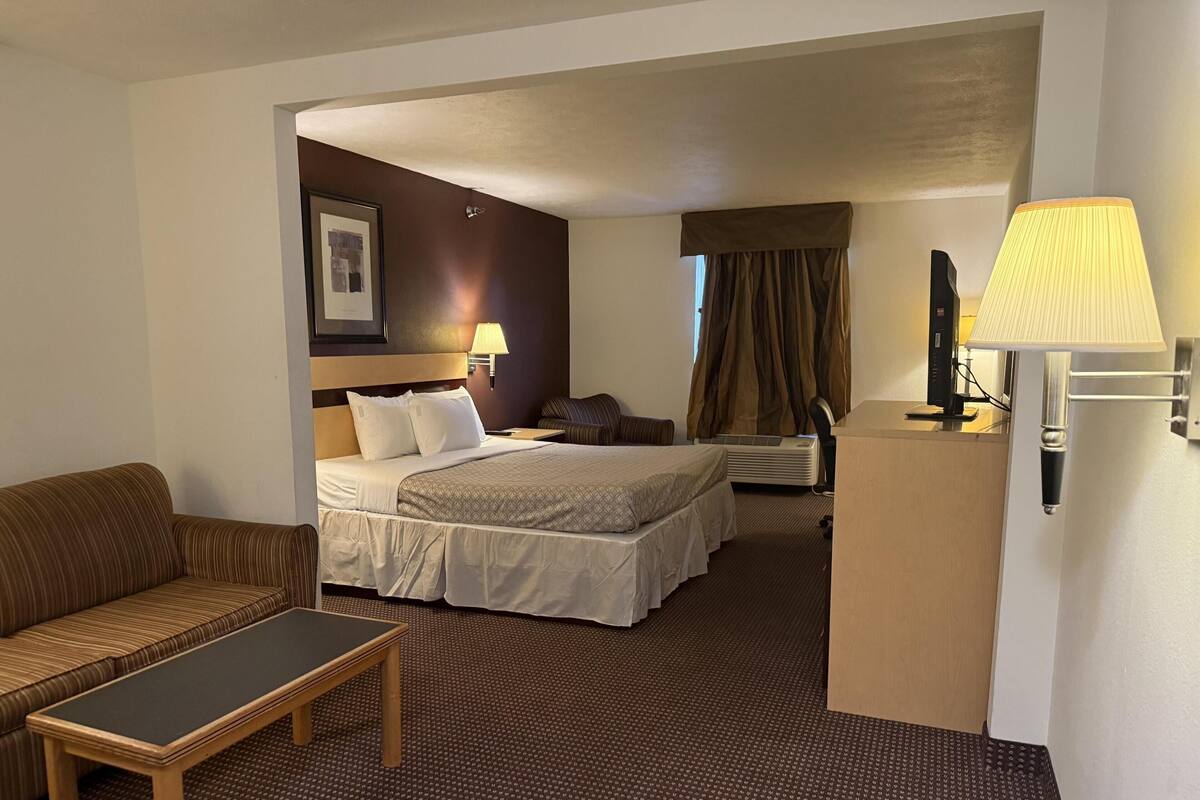 Ein Hotelzimmer mit Bett, Schlafsofa, kleinem Tisch, Schreibtisch, Lampe und einem Bild an der Wand.