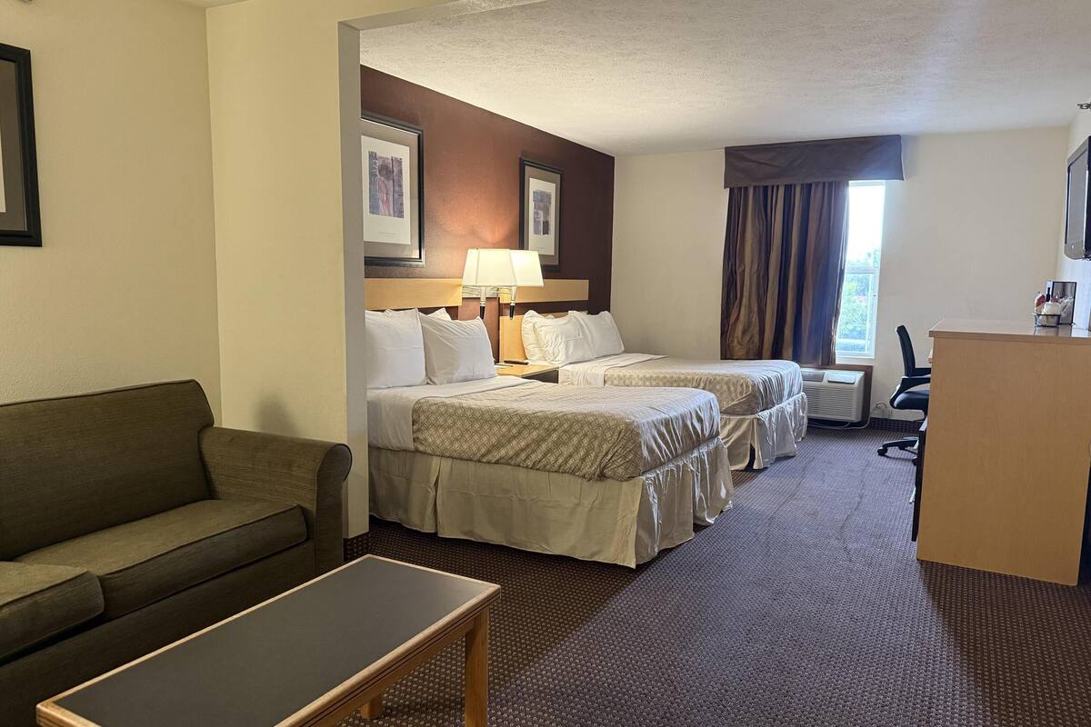 Ein Hotelzimmer mit zwei Betten, einer Couch, einem Schreibtisch und einem Fenster mit Vorhängen.