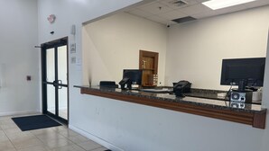 A reception desk with a computer, phone, and a monitor. There is a door with a glass panel and a fire alarm on the wall. - Surestay By Best Western Obetz Rickenbacker Airport (Obetz)