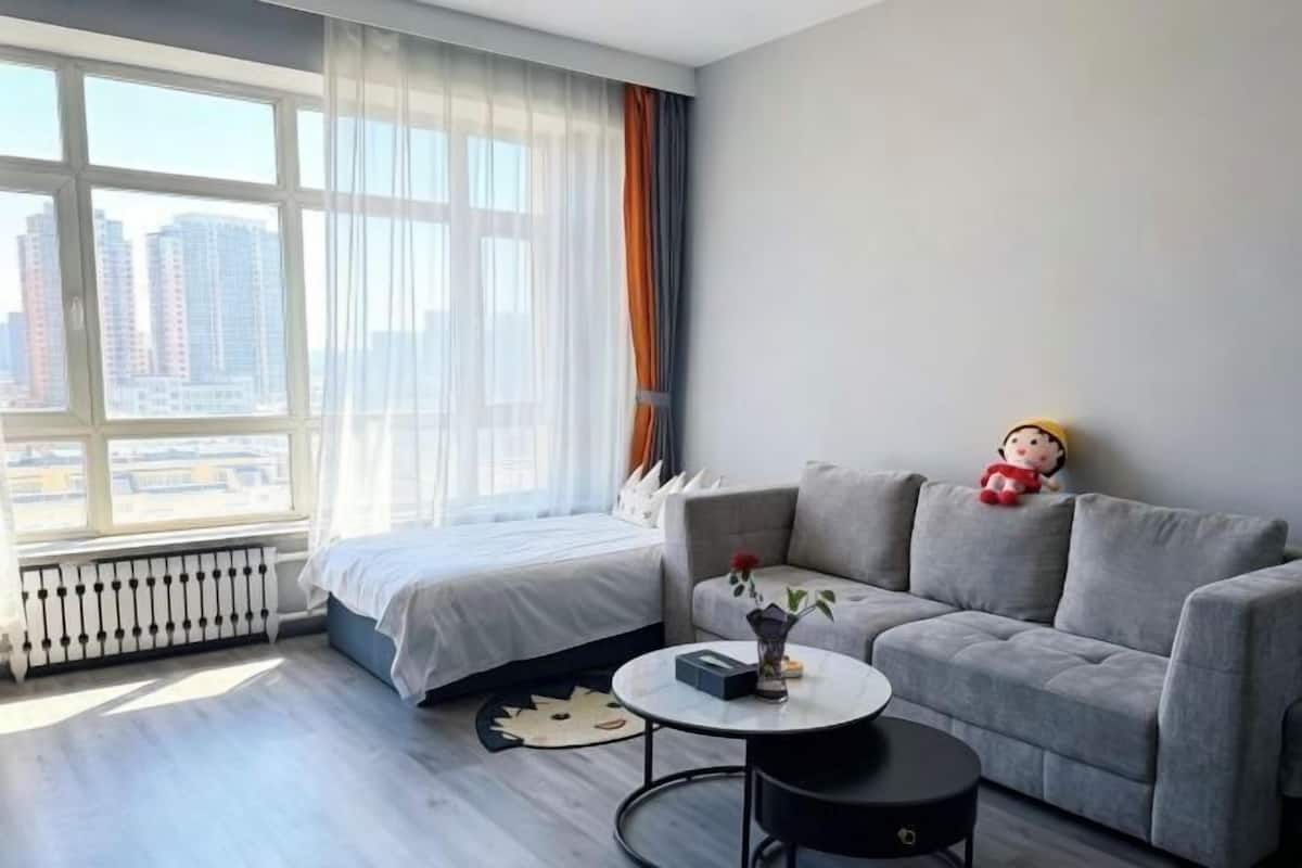 A modern room with a bed, grey sofa, and a small table with a vase.