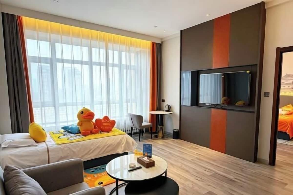A hotel room with a bed, a round coffee table, a TV mounted on the wall, and a window with curtains.