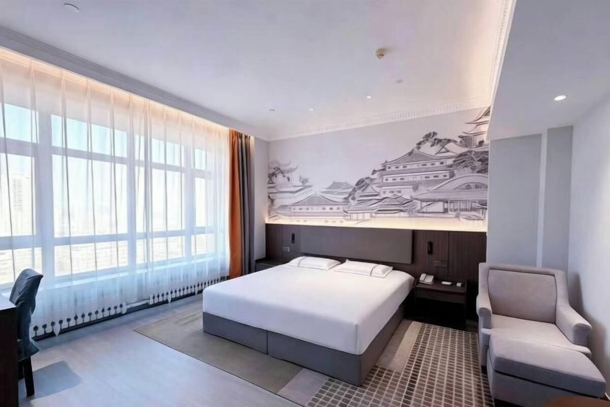A modern hotel room with a large bed, a desk, a chair, and a wall mural.