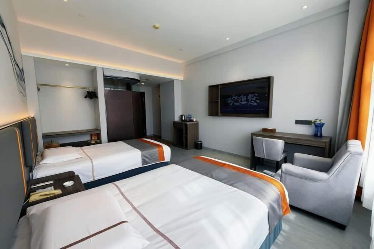 A hotel room with two beds, a desk, a chair, a television, and a bathroom.
