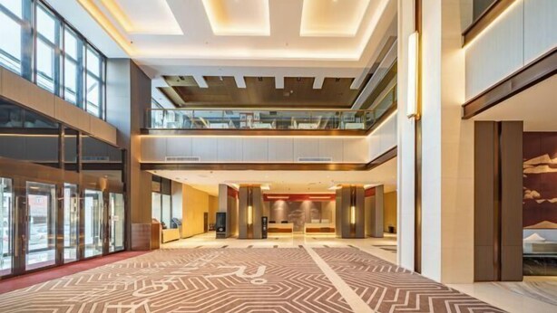 A spacious lobby with a geometric patterned carpet, a mezzanine level, and a reception desk.
