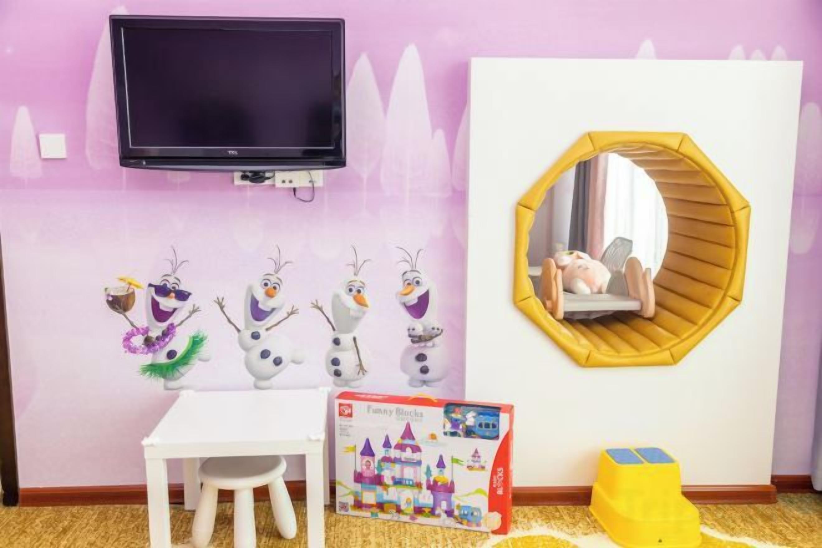 A child's playroom with a TV, a white table, a mirror, and a Frozen-themed toy box.