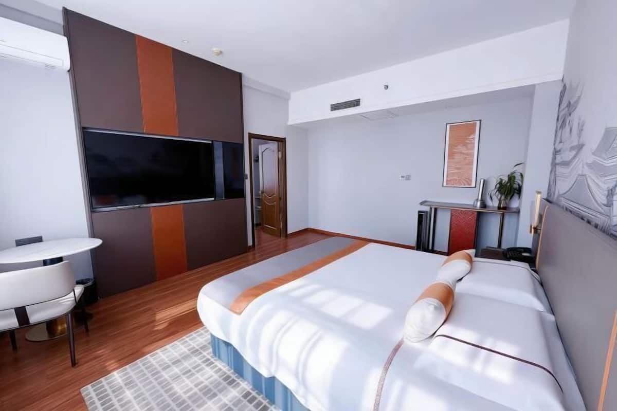 A modern hotel room with a large bed, a desk, a flat-screen TV, and a window.
