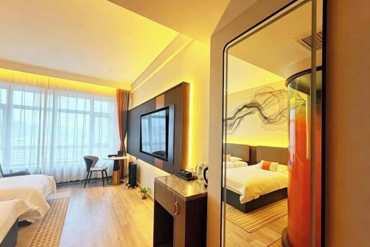 A hotel room with a bed, a desk, a chair, a TV, and a large mirror.