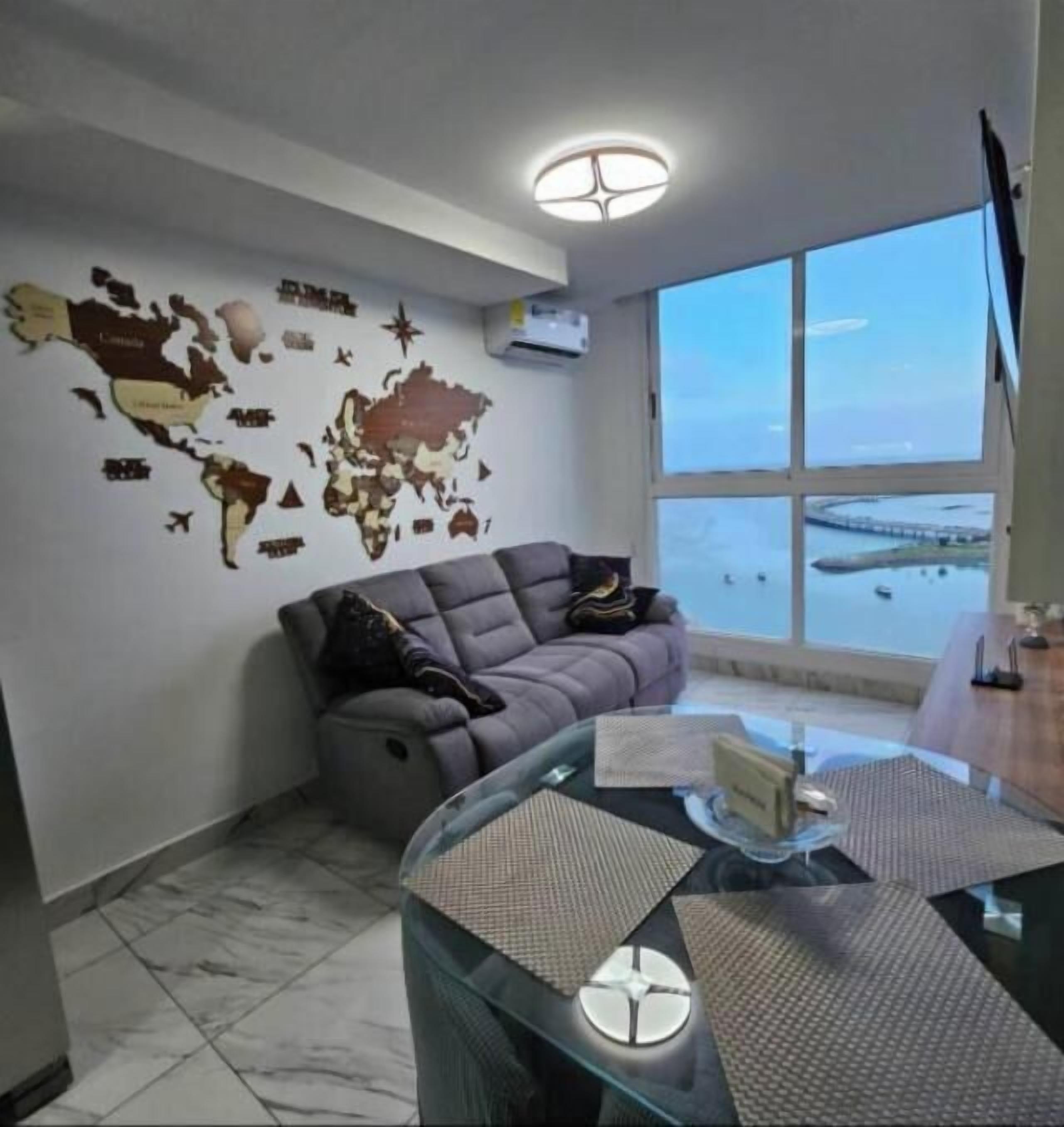 A modern living room with a world map wall decoration, a grey sofa, and a glass coffee table.