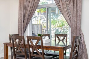 Ein Essbereich mit einem Holztisch und Stühlen, einer Pflanze auf dem Tisch und Blick auf eine felsige Außenlandschaft durch eine Glastür.