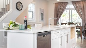 A modern kitchen with a built-in dishwasher, a dining area with a table and chairs, and a staircase leading to another level. - Steps from Trails and Village Shops (Highlands)