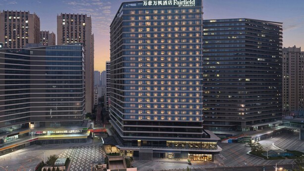 Un hotel moderno con un cartel llamativo, varios pisos y un área de entrada bien iluminada.