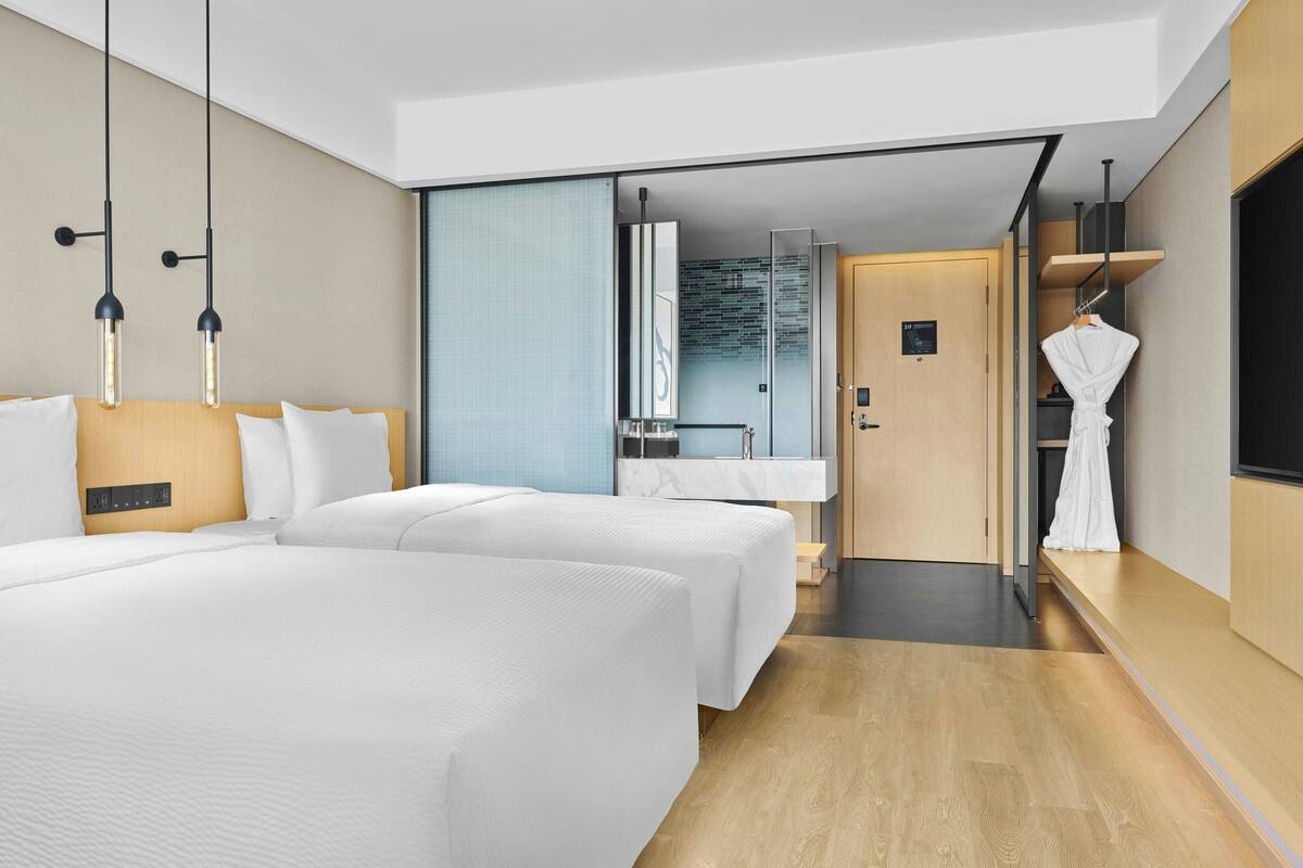 A modern hotel room with two beds, a large mirror, a wooden wardrobe, and a robe hanging on a hook.