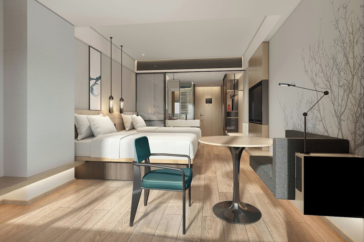 A modern hotel room with a bed, a desk, a chair, a TV, and a bookshelf.