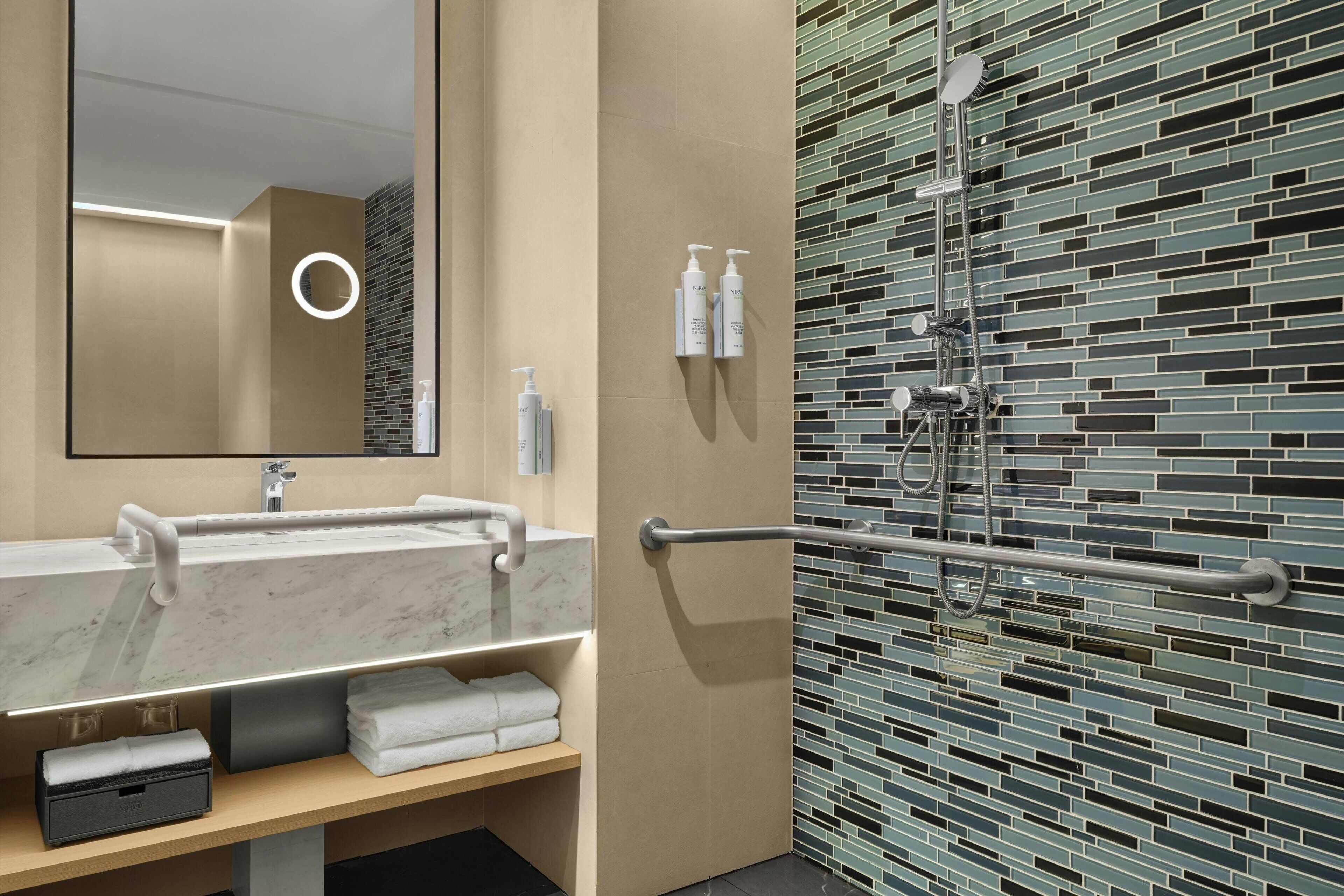 A modern bathroom with a marble sink, a mirror, a towel rack, and a shower with a tiled wall.