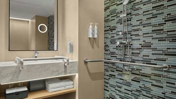 A modern bathroom with a marble sink, a mirror, a towel rack, and a shower with a tiled wall.