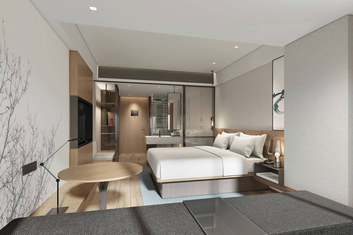 A modern hotel room with a large bed, a round table, and a TV.