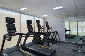 Ein Fitnessraum mit Laufbändern, Crosstrainern und einer Wanduhr.