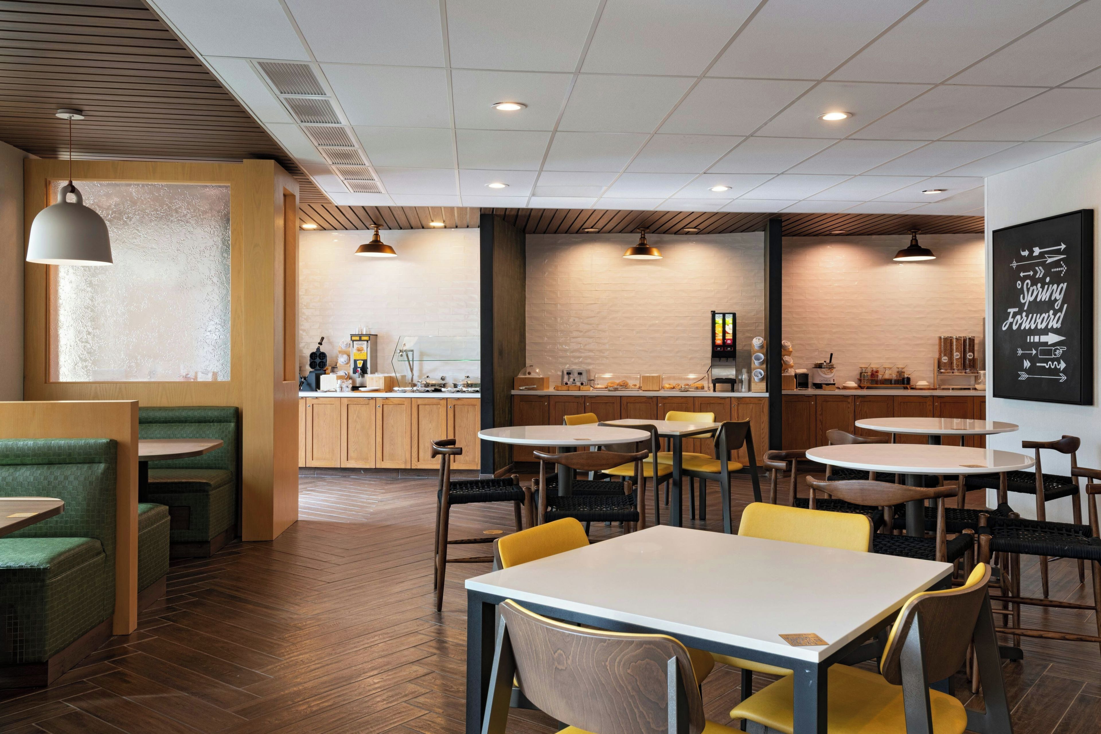 A modern cafe interior with wooden flooring, green and yellow seating, and a visible coffee bar.