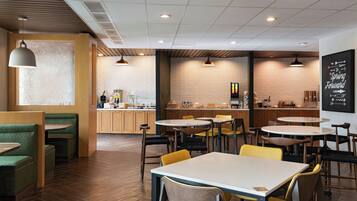 A modern cafe interior with wooden flooring, green and yellow seating, and a visible coffee bar.