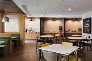 Interior de cafeteria moderna amb sòl de fusta, seients verds i grocs i una barra de cafè ben visible.