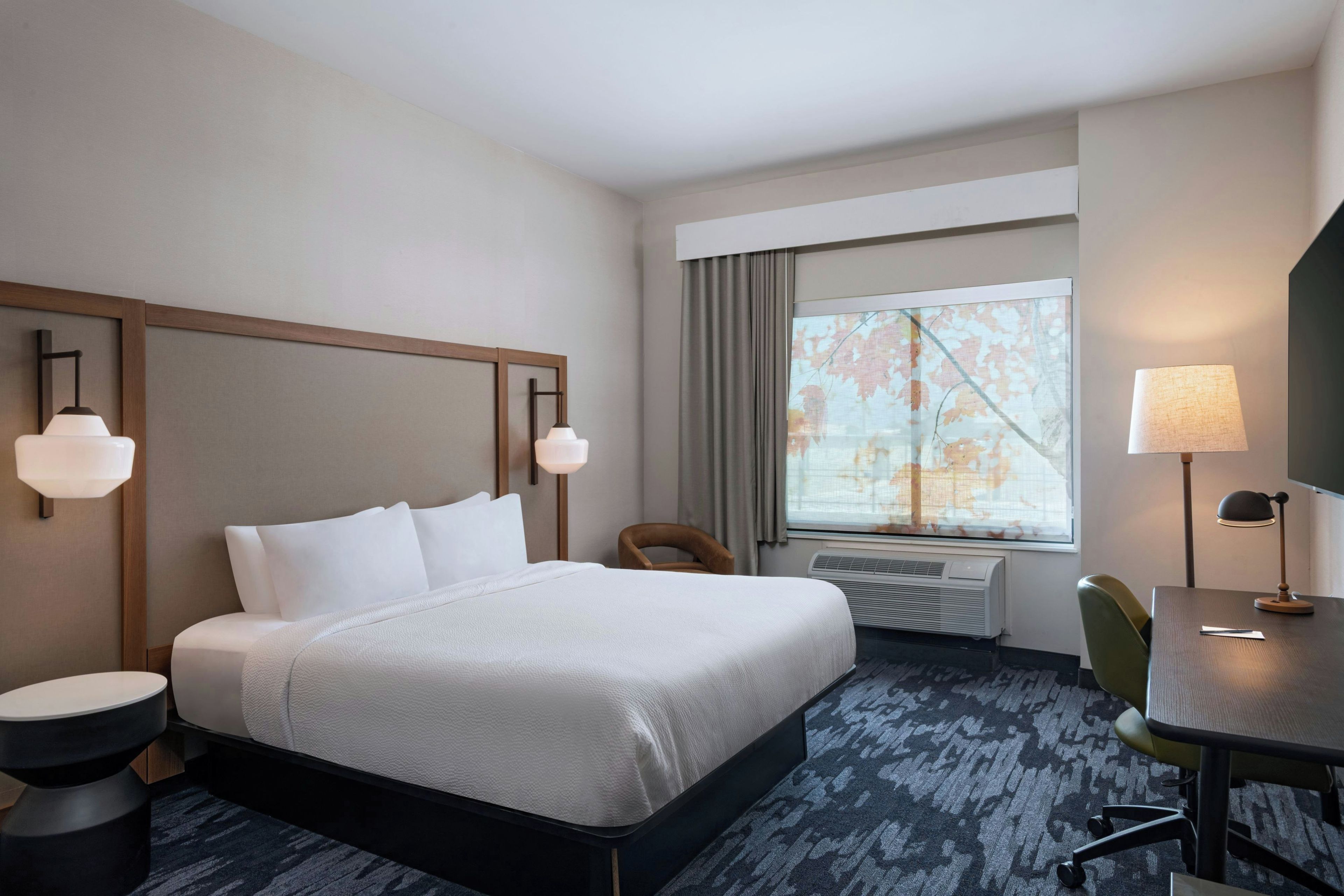 Ein Hotelzimmer mit einem großen Bett, einem Schreibtisch, einem Stuhl, einem Fenster mit Aussicht und einem Wandheizkörper.