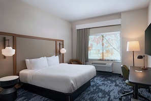 A hotel room with a large bed, a desk, a chair, a window with a view, and a wall-mounted heater.