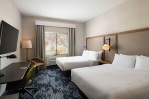 Habitación de hotel con dos camas, un escritorio, una silla, un televisor y una ventana con cortinas.