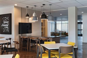A modern restaurant interior with a bar area, seating arrangements, and a large window providing natural light.