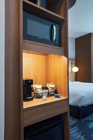 Ein Hotelzimmer mit einer Mikrowelle auf einem Holzregal, einer Kaffeemaschine und einem Tablett mit Kaffeekapseln und Tassen.