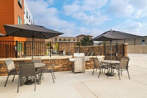 Un patio exterior con una parrilla, mesas, sillas y sombrillas.