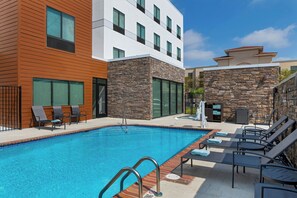 Ein Swimmingpool mit einer Metallleiter, Liegestühlen und einer Steinmauer.