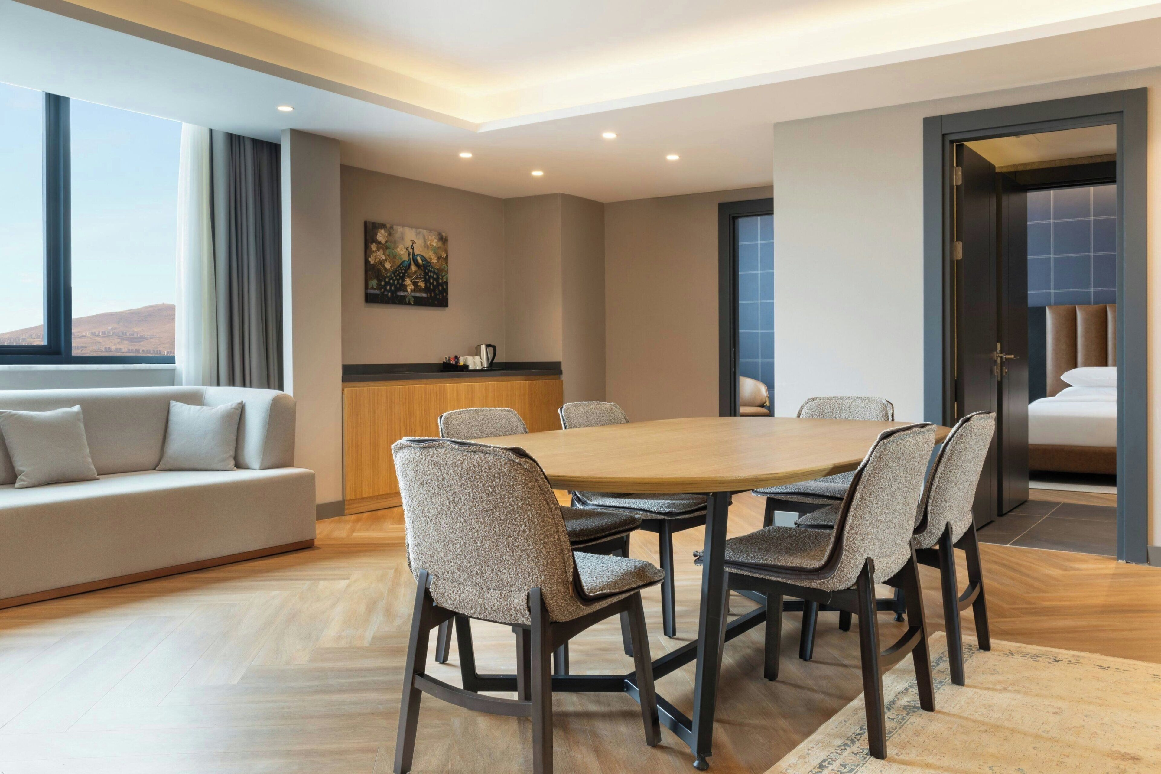 A modern hotel room with a dining area, a sofa, and a painting on the wall.