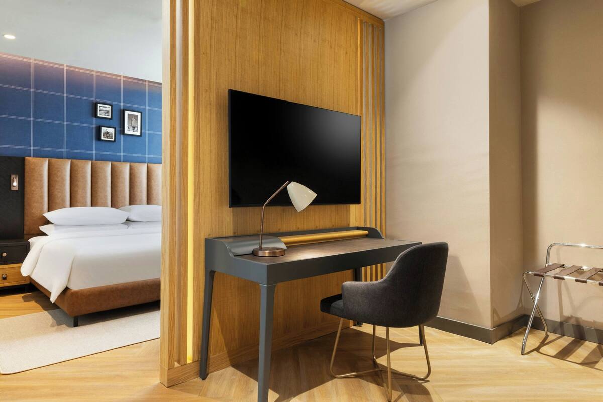 Ett modernt hotellrum med en säng, ett skrivbord, en stol, en TV och en hylla som är monterad på väggen.