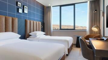 A hotel room with two beds, a desk, and a view of the desert.