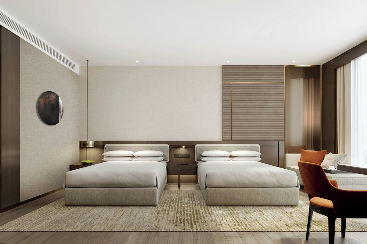A modern hotel room with two beds, a desk, and a chair.