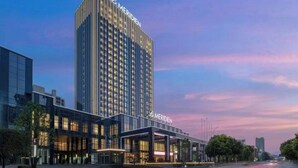 Un hotel moderno con un edificio alto y rectangular, y un anexo más bajo con fachada de vidrio.