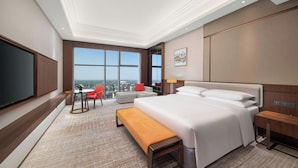 Habitación de hotel con una cama grande, televisión, escritorio, silla y vista a la ciudad.