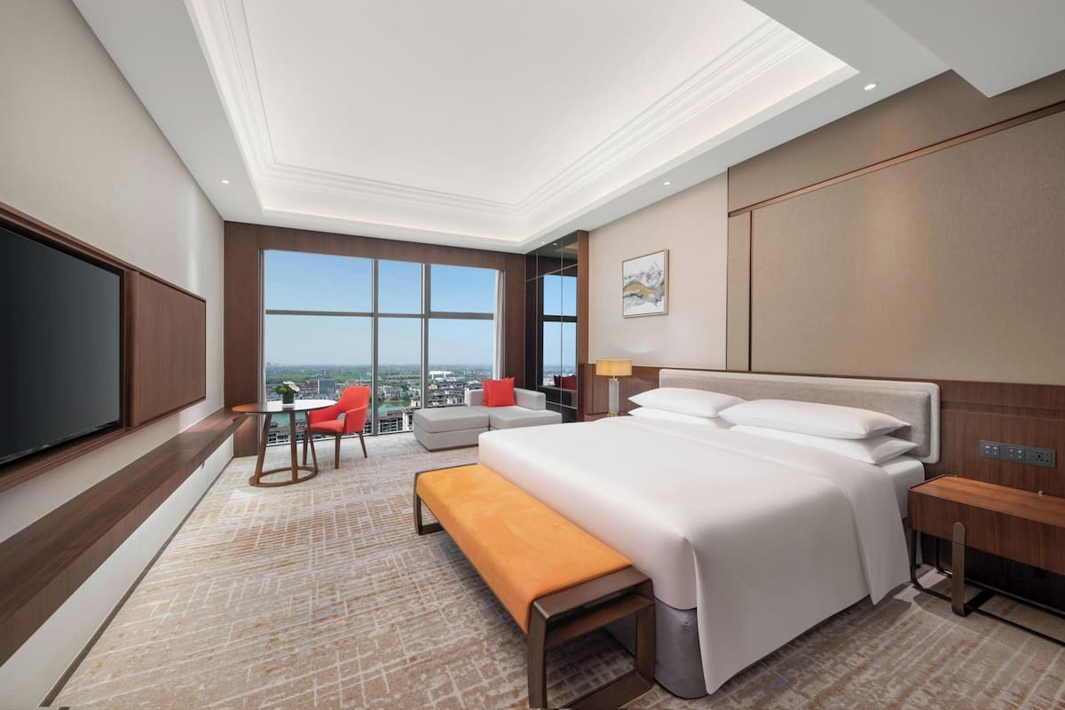 A hotel room with a large bed, a TV, a desk, a chair, and a view of the city.