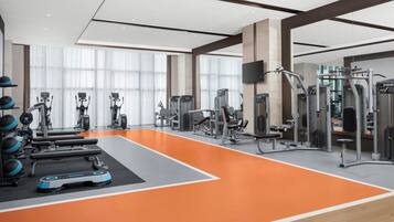 Un gimnasio moderno con diverso equipo de ejercicio, ventanas amplias y un piso de color naranja brillante.