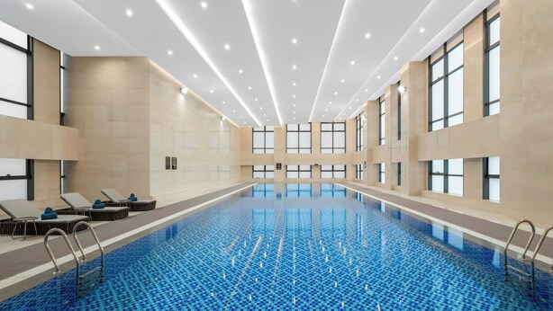 Una amplia piscina interior con agua azul cristalina, rodeada de sillones y tumbonas, con ventanas grandes y un diseño moderno en el techo.