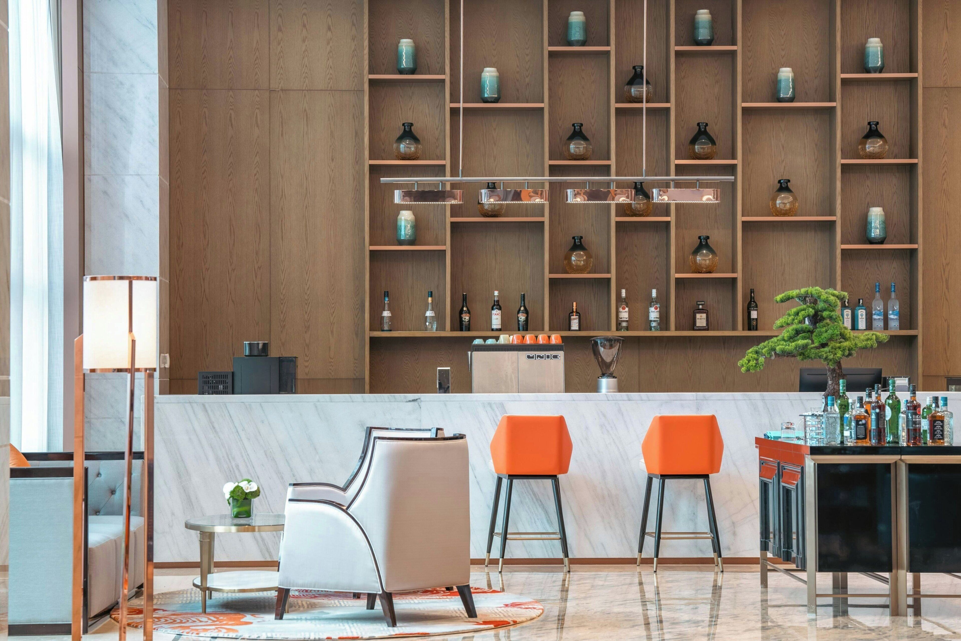A modern bar area with wooden shelves, bar stools, and a marble countertop.
