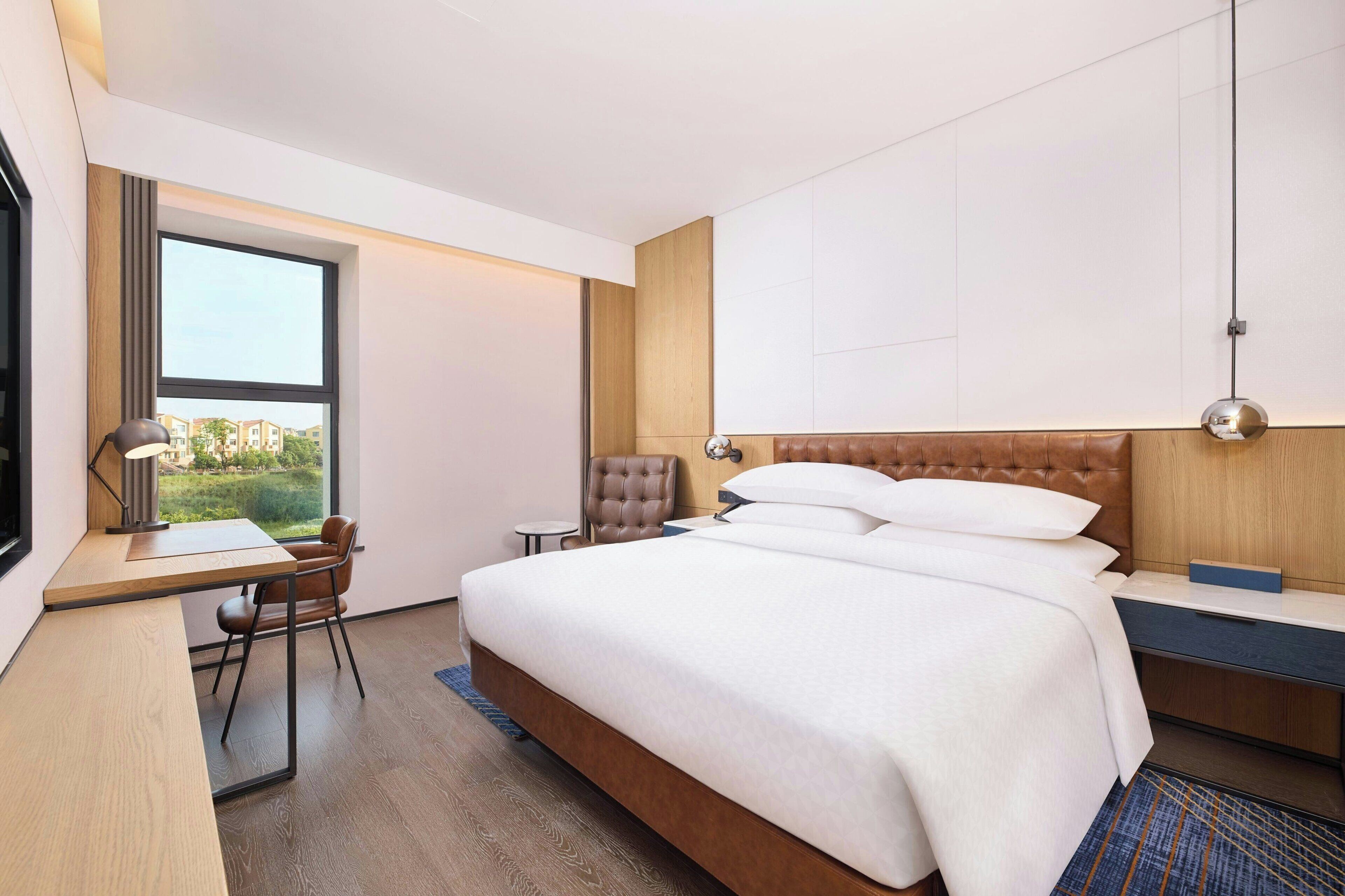 Une chambre d’hôtel moderne, dotée d’un grand lit, d’un bureau, d’une chaise et offrant une vue sur l’extérieur.