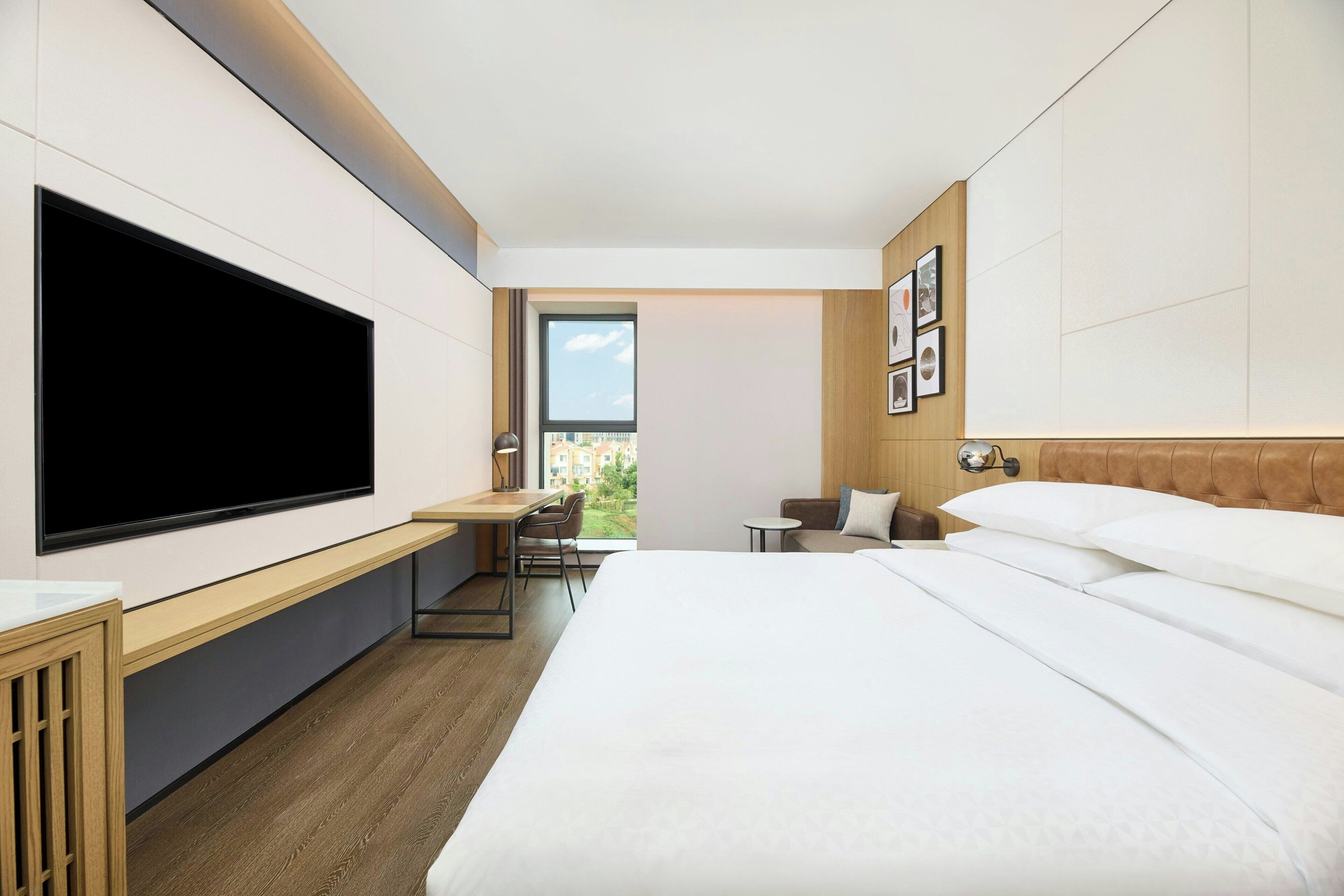 Een moderne hotelkamer met een groot bed, een flatscreen televisie aan de wand, een bureau met een stoel en een klein tafeltje.