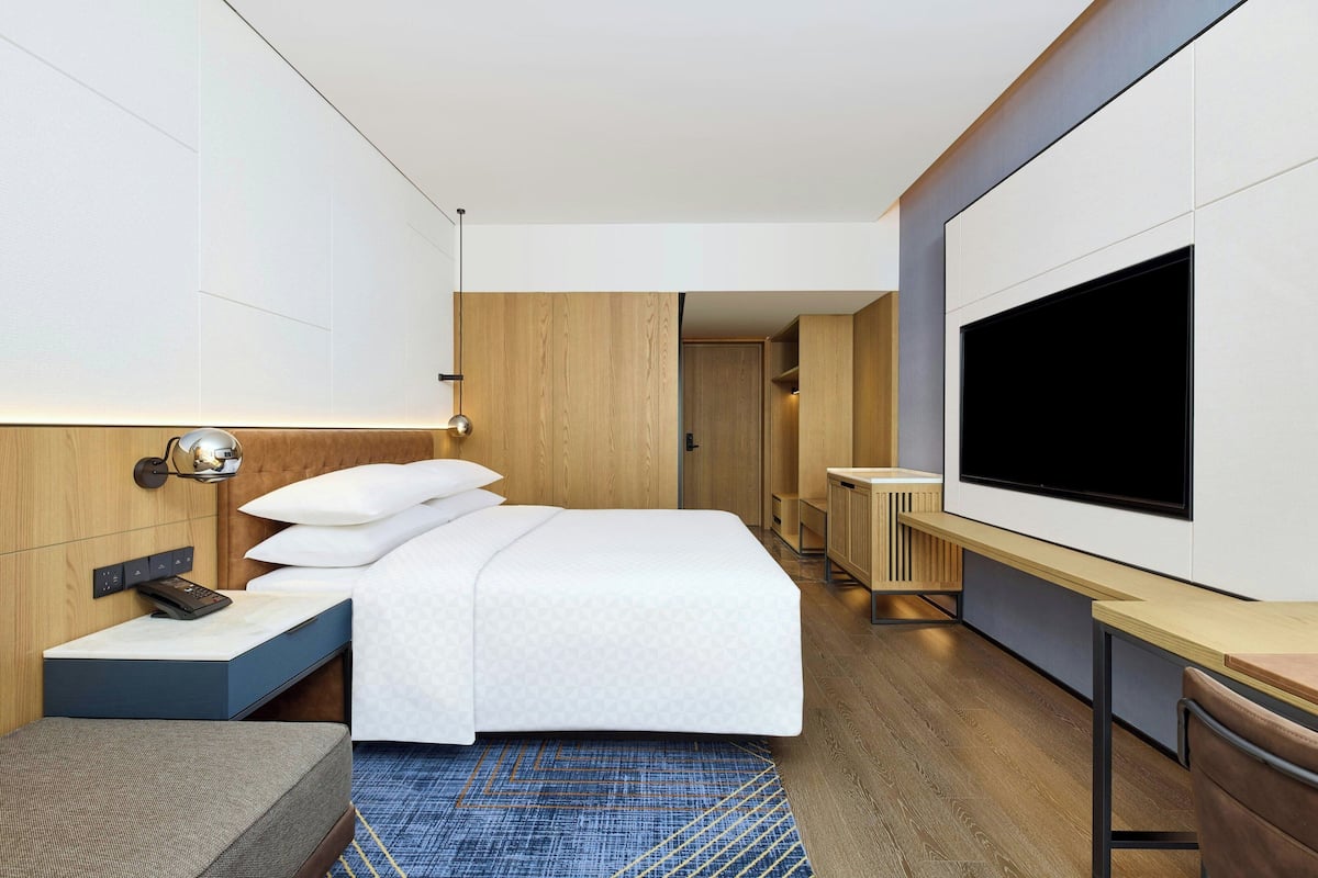 A modern hotel room with a large bed, a desk, a flat-screen TV, and a small seating area.